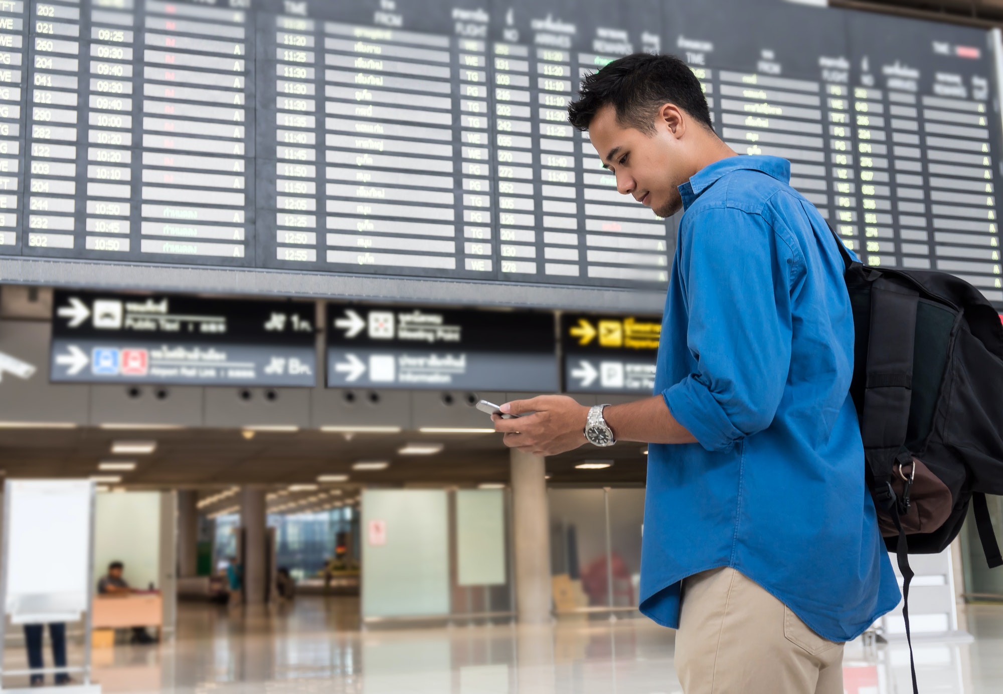 Asian traveler using the smart mobile phone for check-in at the flight information screen