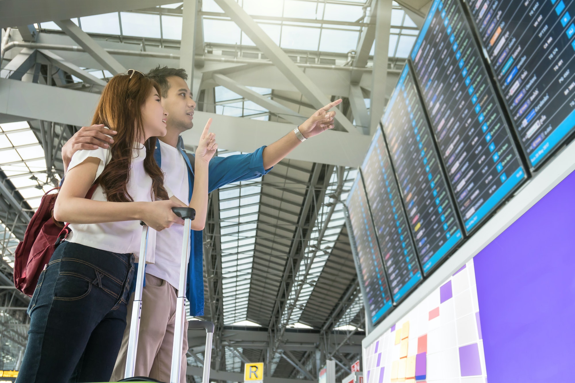 Asian woman traveler with suitcases pointing at the flight information screen